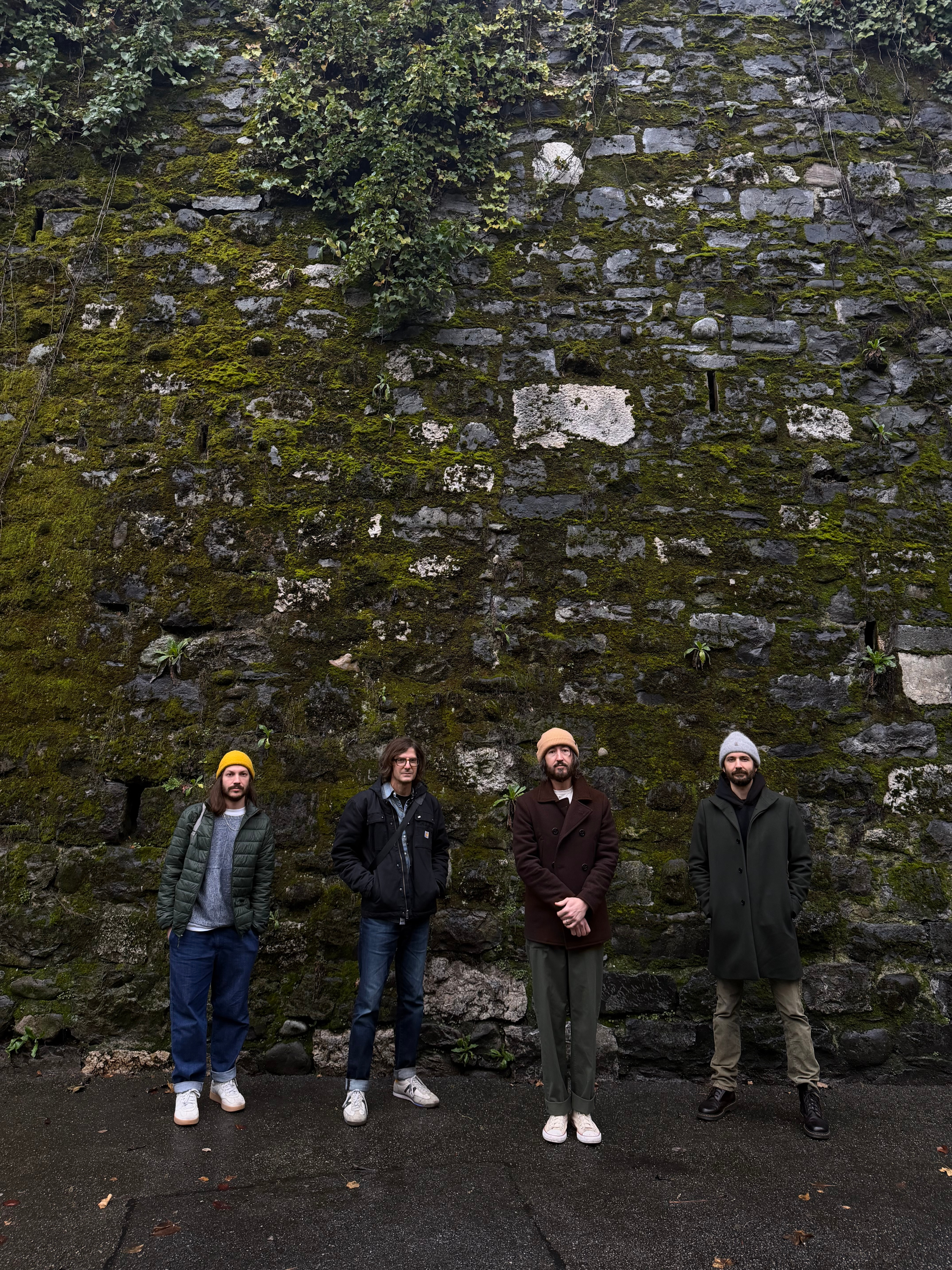 The Bretheren standing together in front of a moss-covered stone wall